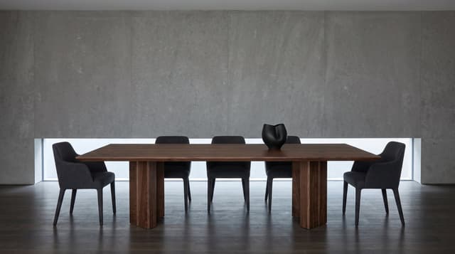 The Vekt Walnut Dining Table in a gallery-like room, a limestone wall with a slot window, charcoal wool chairs