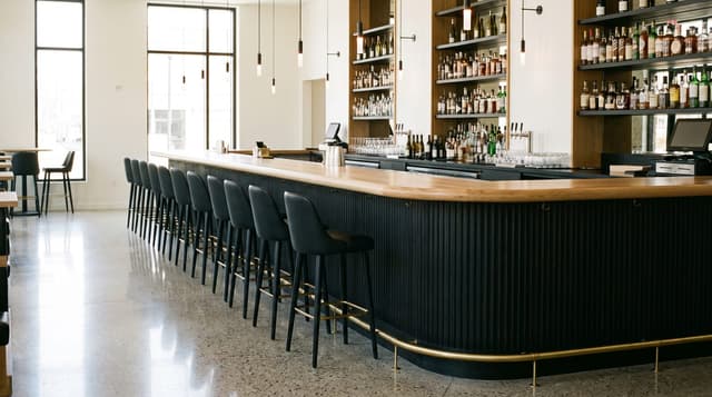 Long white oak bar top with a roundover edge on a fluted black bar front with a brass foot rail