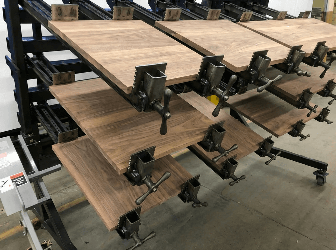Walnut tabletops in the glue rack during fabrication, showing panel alignment and early stages of construction