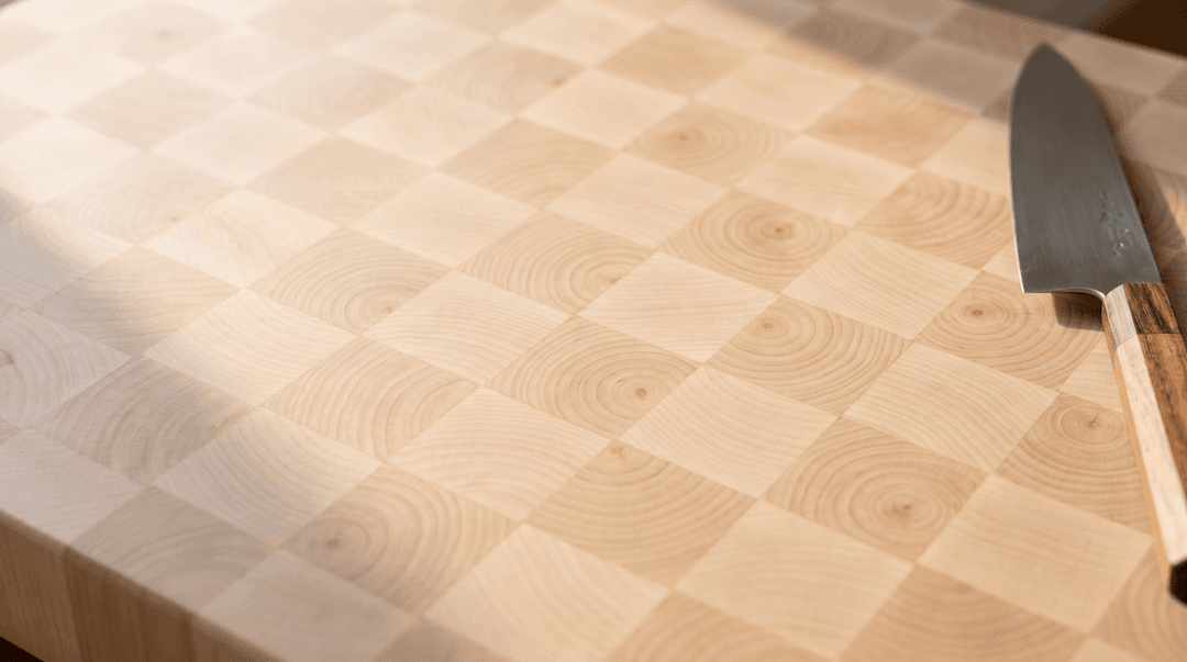 End grain hard maple butcher block — pale checkerboard of upturned blocks with a chef’s knife resting on it