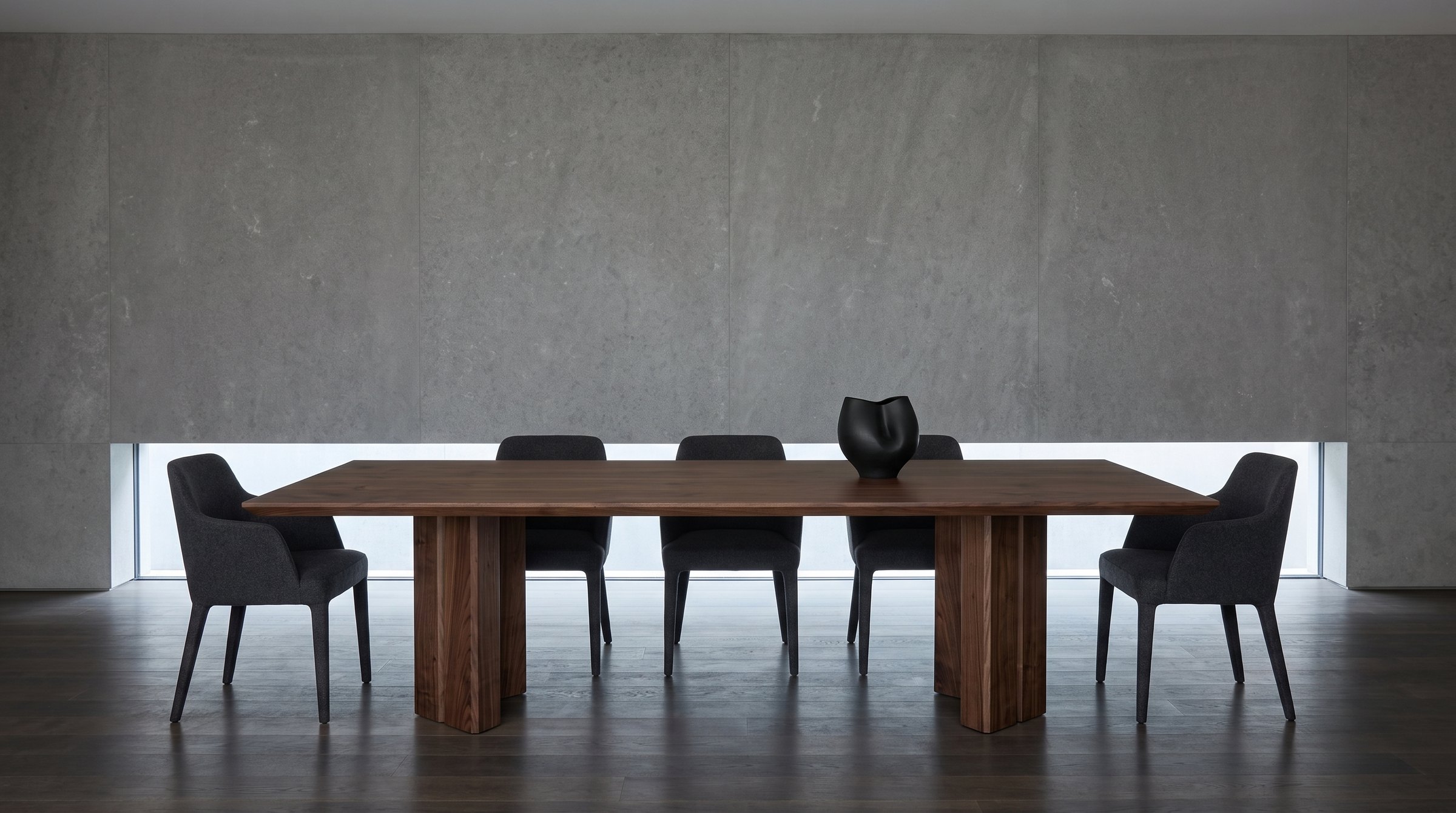 Solid walnut dining table, face grain — the Vekt Walnut Dining Table in a gallery-like room, a limestone wall with a slot window, charcoal wool chairs
