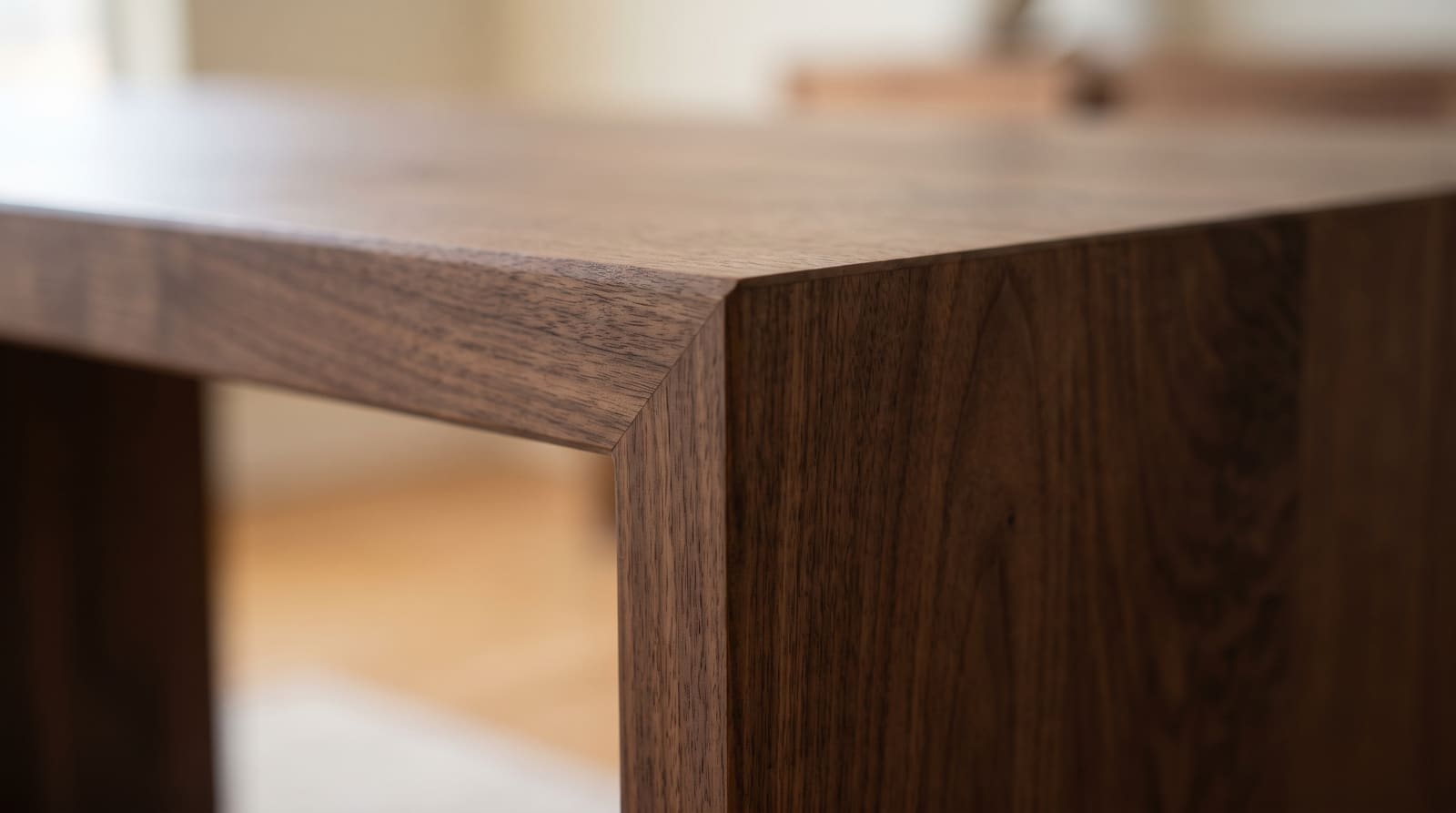 Solid walnut tabletop, face grain — close-up of a walnut waterfall corner, the miter closed to a hairline